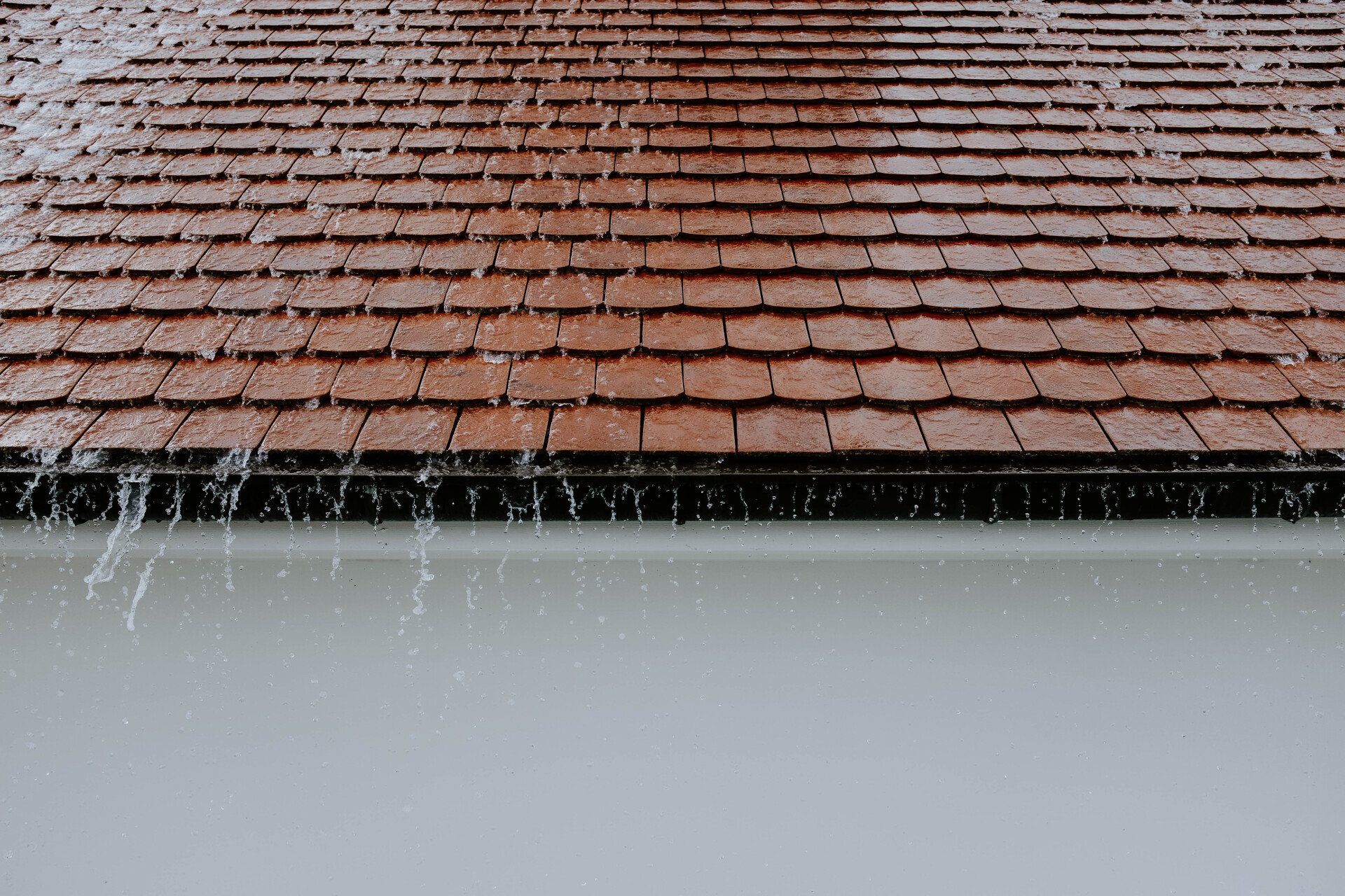 Rainwater spilling from a red tiled roof over a white wall